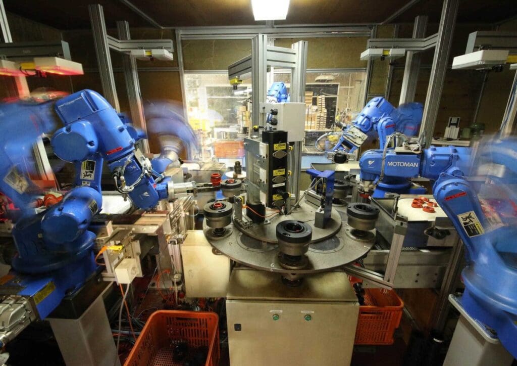 Automated robotic assembly cell with multiple blue industrial robots assembling Philmac components on a rotating indexing table inside a controlled manufacturing enclosure